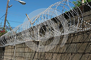 Barbed wire at top of a high, grey, brick wall protecting entrance to private property in Kingston, Jamaica.