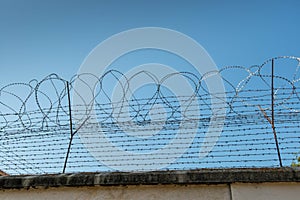 Barbed wired fence on jail wall against perfect blue sky