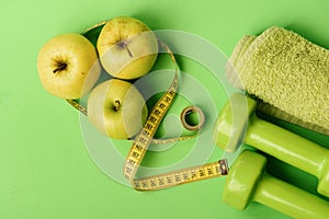 Barbells by juicy green apples. Diet and sport regime concept. Dumbbells in bright green color, twisted measure tape