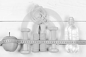 Barbells, jump rope, bottle and apple on wooden background