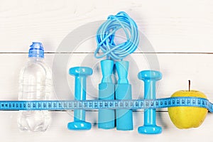 Barbells, jump rope, bottle and apple on wooden background