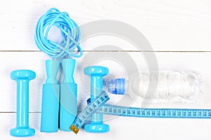 Barbells, jump rope, centimeter and bottle on wooden background