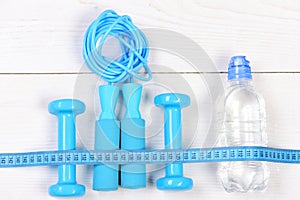 Barbells, jump rope, long centimeter and bottle on wooden background