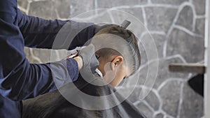 Barber in black gloves carefully shaves the nape of an Asian child in a barber shop, close up 60 fps