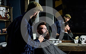 Barber busy with grooming beard of hipster client, mirror reflexion on background. Grooming concept. Hipster with beard