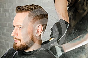 The barber cleans the neck of an adult man with a brush with talc after a haircut on a white brick wall background