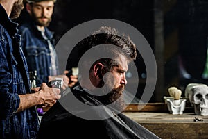 Barber with clipper styling hair of brutal bearded client. Hipster lifestyle concept. Barber with hair clipper works on