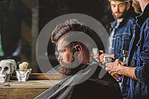 Barber with clipper styling hair of brutal bearded client. Hipster lifestyle concept. Barber with hair clipper works on