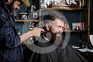 Barber with clipper trimming hair on nape of client. Barber with hair clipper works on haircut of bearded guy barbershop