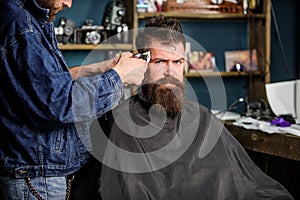 Barber with clipper trimming hair on temple of client. Hipster lifestyle concept. Barber with hair clipper works on