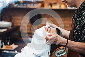 Barber covers the face of a man with a hot towel. Traditional ritual of shaving the beard with hot and cold compresses in a old