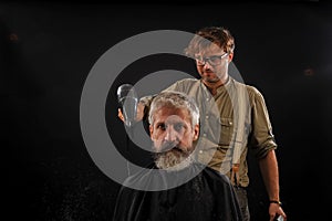 Barber cuts a beard to a client to an elderly gray-haired