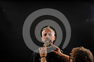 Barber cuts a beard to a client to an elderly gray-haired man