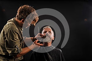 Barber cuts a beard to a client to an elderly gray-haired man