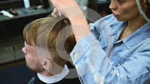 The barber cuts a bearded man with scissors in the salon