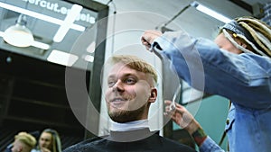 The barber cuts a bearded man with scissors in the salon