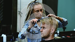 The barber cuts a bearded man with scissors in the salon