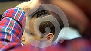 Barber cuts the boy`s hair. The process of forming a haircut close-up.