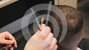 Barber cuts client hair with comb holding scissors in shop