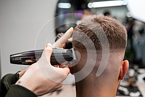 Barber cuts client short hair with trimmer in barbershop