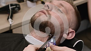 Barber cuts straight beard contour on man neck in barbershop