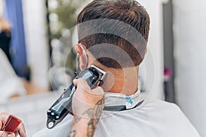 Barber cutting the hair of the nape of a man using an electric machine