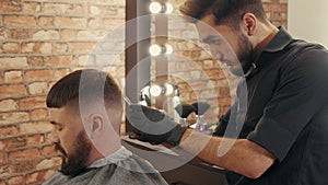 Barber cutting hair to bearded male client in barbershop