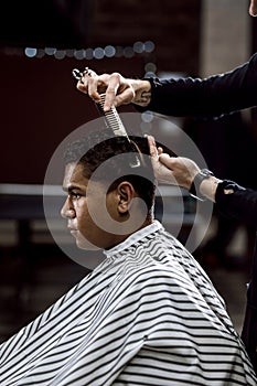 The barber is cutting a man`s hair holding scissors and comb in his hands opposite the mirror in a barbershop