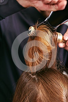 Barber dries the hair with the hair dryer of young, beautiful girl in a beauty salon