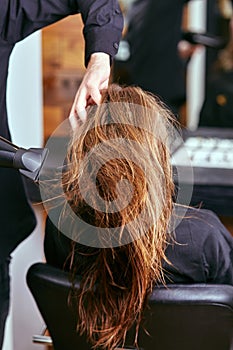 Barber dries the hair with the hair dryer of young, beautiful girl in a beauty salon photo