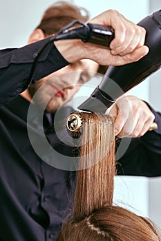 Barber dries the hair with the hair dryer of young, beautiful girl in a beauty salon photo