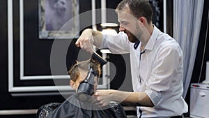 Barber dries hair teenager with a hair dryer.
