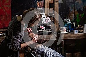 Barber girl shaves his beard with a dangerous razor. Women barber shaves his beard. Barber woman shaving a bearded man