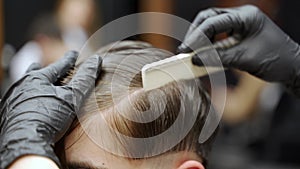 Barber in gloves styles clients hair with comb in professional barbershop. Precision cut, hairdresser maneuvers scissors