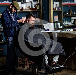 Barber with hair clipper works on haircut of bearded guy barbershop background. Hipster client getting haircut. Barber