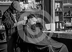 Barber with hair clipper works on haircut of bearded guy, retro barbershop background. Hipster hairstyle concept