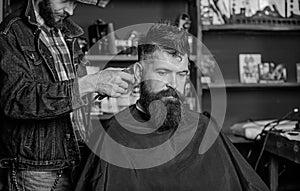 Barber with hair clipper works on hairstyle for bearded guy barbershop background. Hipster client getting haircut