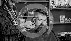 Barber with hair clipper works on hairstyle for bearded guy barbershop background. Hipster lifestyle concept. Barber