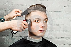 Barber hair styling of young guy in the barbershop on brick wall background, hairdresser makes hairstyle for a young man.