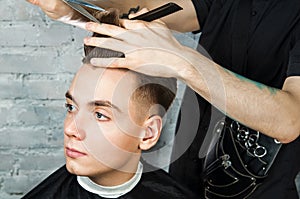 Barber hair styling of young guy in the barbershop on brick wall background, hairdresser makes hairstyle for a young man.
