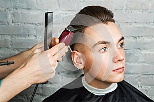 Barber hair styling of young guy in the barbershop on brick wall background, hairdresser makes hairstyle for a young man.