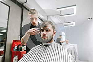 Barber haircuts a handsome hairy man in a light men`s hairdresser, the client looks forward, the hairdresser is working on a hair