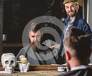Barber and hipster client with beard checking haircut in mirror, dark background. Hipster and barber talking during