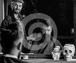 Barber and hipster client with beard checking haircut in mirror, dark background. Hipster and barber talking during