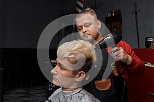 Barber man stylish with a beard Caucasian professional dries hair for a client guy with a hairdryer in a haircut at work in a