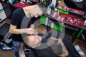 Barber master is shaving of handsome mature bearded man in salon. Hair artist making hairstyle for person in barbershop. Services