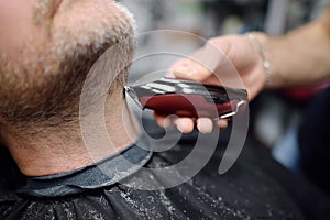 Barber master is shaving of handsome mature bearded man in salon. Hair artist making hairstyle for person in barbershop. Services