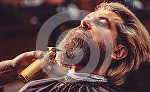 Barber preparing hair clipper for bearded man, barbershop background. Barber works with a beard clipper. Hipster client