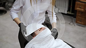 Barber preps man for shave with steamy towel in salon. Male relaxation pre-shaving ritual, wrapping face for skin