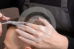 The Barber`s hand with a pair of scissors for cutting the hair of a young man. Creating a stylish men`s haircut in a barbershop.